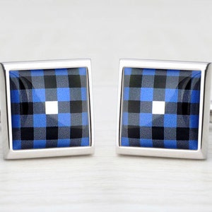 Op de afbeelding: Een paar vierkante manchetknopen met een zilverkleurig metalen frame. Het midden van elke manchetknop heeft een blauw, zwart en wit ruitpatroon. Klassiek, formeel ontwerp.