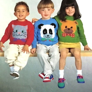 May include: Three children wearing colorful sweaters with animal designs. The sweaters feature a cat, a panda, and a bear. The children are sitting on a wooden surface.