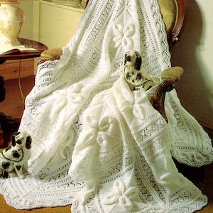 May include: A white crocheted blanket with a delicate floral pattern draped over a wooden chair. The blanket features intricate lacework and a raised flower design.
