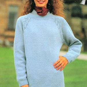 Puede incluir: Un suéter de punto azul claro con cuello redondo y detalles de encaje en los hombros. El suéter está hecho de un material suave y cómodo y tiene mangas largas.