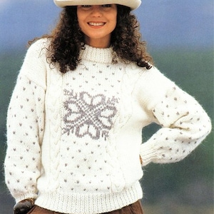 May include: A white knitted jumper with a grey snowflake design and a white dot pattern. The jumper has a round neckline and long sleeves.