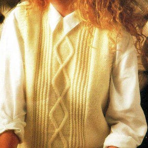 Puede incluir: Un chaleco de punto de color crema con un patrón de trenza. El chaleco tiene cuello en V y se lleva sobre una camisa blanca.