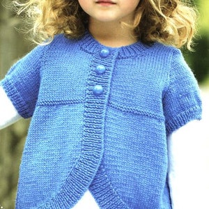 May include: A blue knitted cardigan with a button closure and short sleeves. The cardigan is worn by a young girl with curly blonde hair.