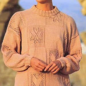 May include: A pale pink knitted sweater with a geometric pattern of hearts and squares. The sweater has a round neckline and long sleeves.