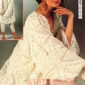 Op de afbeelding: Witte gebreide jas met een kantboord. De jas heeft een textuurrijk breiwerk met grote motieven en reliëfbladeren. "White Magic" staat in grote letters onderaan de afbeelding.