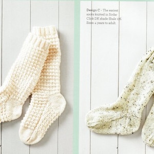 May include: Two pairs of knitted socks in white. The socks on the left have a textured pattern. The socks on the right have a speckled pattern. The text "Design C - Textured socks Knitted in Sirdar Country Style DK shade Palest Pink 391. Sizes: 4 years to adult." is visible on the left side of the image. The text "Design C - The easiest socks knitted in Sirdar Click DK shade Shale 176 Sizes: 4 years to adult." is visible on the right side of the image.