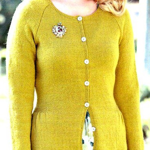 May include: Mustard yellow cardigan with a round neckline and long sleeves. The button-down sweater features a decorative brooch and is paired with a floral print skirt. The cardigan is a classic piece of clothing.