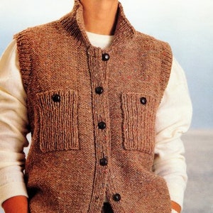 Op de afbeelding: Een bruin gebreid vest met een knoopsluiting en twee klepzakken. Het vest heeft een hoge kraag en is mouwloos.