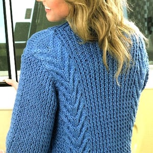 May include: A blue knitted cardigan with a cable knit pattern on the back. The cardigan has a relaxed fit and a cropped length.