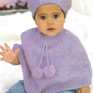 May include: A purple knitted poncho with a matching beret. The poncho has a tie at the neck and two pom-poms at the bottom. The beret has a small amount of white and pink flecks in the yarn.