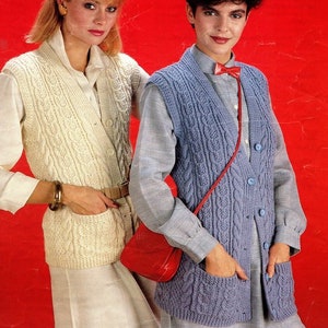 May include: Two women wearing knitted vests. The vest on the left is white and the vest on the right is blue. Both vests have a cable knit pattern and button closures.