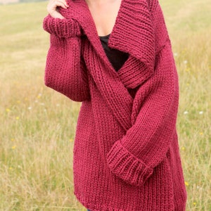 Op de afbeelding: Een diep rode gebreide cardigan met een brede, gevouwen kraag en lange mouwen. De cardigan is gemaakt van een zacht, dik garen en heeft een ontspannen pasvorm.