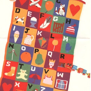May include: A colorful knitted alphabet blanket with a variety of images for each letter. The blanket is made with different colored squares and features a teddy bear, airplane, balloon, cat, heart, dog, egg, feather, fence, hat, ice cream cone, pitcher, kite, lollipop, mitten, needle, orange, pear, queen, train, sock, teddy bear, umbrella, dress, window, ladder, sailboat, and zipper.