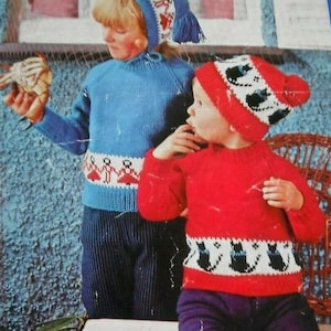 Puede incluir: Dos niños con suéteres y gorros de punto. Uno lleva un suéter y gorro azules con un patrón blanco y rojo. El otro lleva un suéter y gorro rojos con un patrón blanco y negro. Los suéteres tienen bandas estampadas.