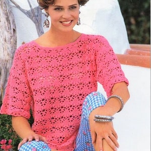 May include: A pink crocheted top with a lacy pattern. The top has a round neckline and short sleeves. The model is wearing the top with blue and white checkered pants.