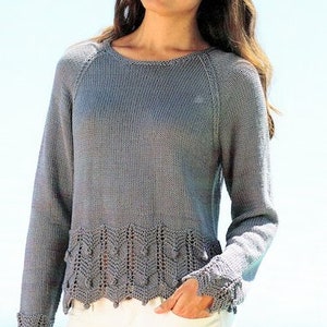 以下が含まれることがあります： 長袖と丸首のグレーのニットセーター。セーターは装飾的なスカラップの裾と袖口が特徴です。白いパンツを履いています。背景は水色です。