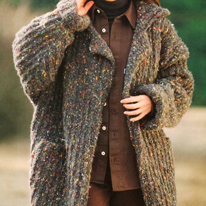 Könnte beinhalten: Ein langer, brauner und grauer Strickcardigan mit einem gesprenkelten Muster. Der Cardigan hat einen Schalkragen und Taschen. Der Cardigan wird über einem braunen Hemd mit weißem Kragen getragen.