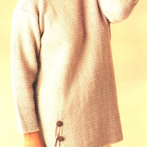 May include: A light beige knit sweater with a textured pattern. The long-sleeved sweater has a round neckline and two brown buttons on the side. The sweater is a loose fit.