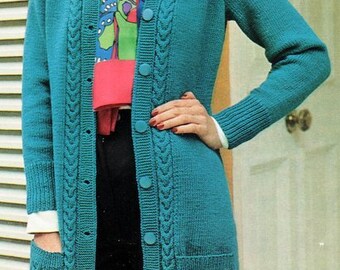 Op de afbeelding: Een tealblauwe gebreide cardigan met een kabelbreipatroon, lange mouwen en een knoopsluiting. De cardigan heeft twee klepzakken aan de voorkant en een witte kraag.