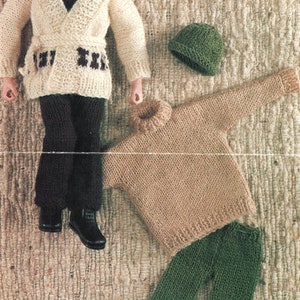 Puede incluir: Un conjunto de ropa de punto para muñeca, que incluye una chaqueta blanca de punto con ribetes marrones, un jersey marrón de cuello alto, pantalones verdes y un gorro verde.