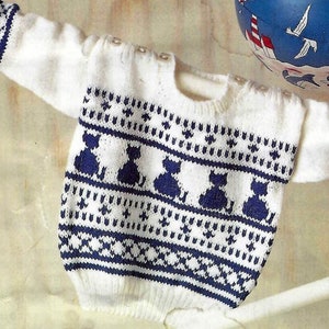 May include: White knitted baby sweater with a blue and white pattern of cats. The sweater has a crew neck and long sleeves.