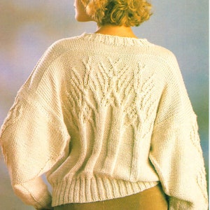 Könnte beinhalten: Ein cremefarbener Strickpullover mit einem Zopfmuster. Der Pullover hat lange Ärmel und eine lockere Passform.