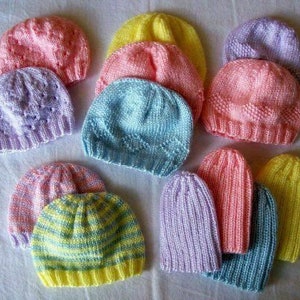 Puede incluir: Una colección de 11 gorros de punto para bebé en varios colores, incluyendo rosa, azul, amarillo y morado. Los gorros están hechos con diferentes patrones y texturas de punto.