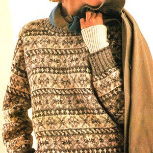 Può includere: Una donna indossa un maglione a motivi marroni e bianchi con un cappello marrone e un cappotto marrone.