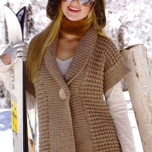 May include: A brown knitted cardigan with a large collar, a single button closure, and short sleeves. The cardigan is worn by a person holding a ski.