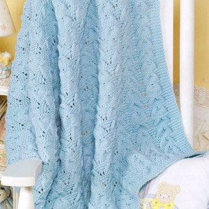 May include: A light blue knitted baby blanket with a delicate cable stitch pattern. The blanket is draped over a white rocking chair.