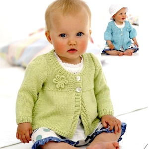 Peut inclure: Un bébé portant un cardigan en tricot vert clair avec un détail de fleur et des boutons blancs. Le cardigan a un col rond et des manches longues.