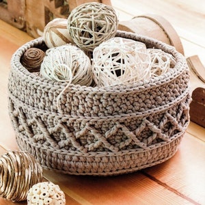 Puede incluir: Una cesta de crochet de color beige, llena de bolas decorativas blancas y marrones. La cesta tiene un diseño texturizado con un patrón trenzado.