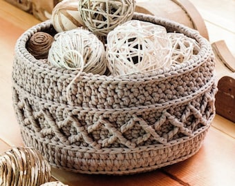 May include: A crocheted basket with a beige color, filled with white and brown decorative balls. The basket has a textured design with a braided pattern.