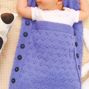 Könnte beinhalten: Ein lila gestrickter Schlafsack für Babys mit einer passenden Kapuze. Der Schlafsack hat eine Reihe von Knöpfen an der Seite.