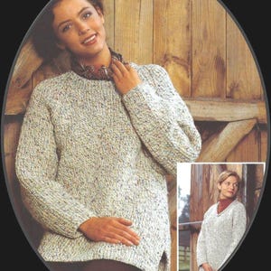 May include: A light grey sweater with a speckled pattern. The sweater has a round neckline and long sleeves. The sweater is shown on a model standing in front of a wooden barn door.