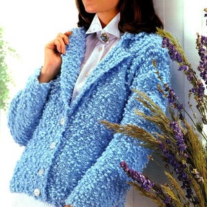 May include: A light blue knitted cardigan with a collar and button fastening. The cardigan is made with a textured yarn that creates a fuzzy look. The model is wearing a white collared shirt underneath the cardigan.