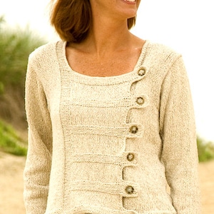 May include: A cream-colored knitted sweater with a unique asymmetrical design and button closures. The sweater has a scoop neck and long sleeves.