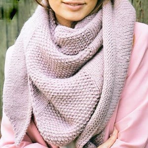 May include: A soft, pink knitted scarf with a textured stitch pattern. The scarf is folded and draped around the neck of a person wearing a pink shirt.