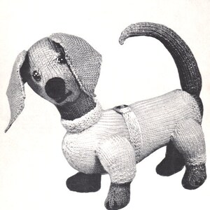 May include: A knitted gray and white dachshund dog toy. The dog is wearing a white sweater with a button detail.
