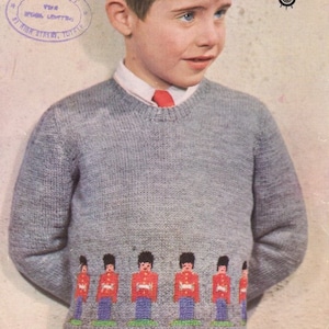 May include: A gray knitted sweater with a row of red, blue, and white toy soldiers across the bottom. The sweater has a crew neck and long sleeves.