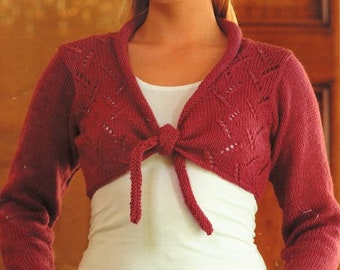 May include: A red knitted shrug with a tie front and leaf-like lace detail. The shrug is shown on a model wearing a white t-shirt and blue jeans. 81 - 107 cm, 32 - 42 in.