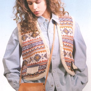 May include: A woman wearing a blue button-down shirt with a white and multi-coloured knitted waistcoat. She is carrying a brown leather shoulder bag.