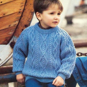 May include: A blue knitted jumper with a cable knit pattern. The jumper has a round neckline and long sleeves.