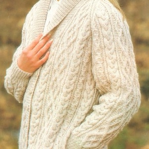 May include: A cream-coloured cable knit cardigan with a shawl collar and a zip fastening. The cardigan has a pocket on the left side.