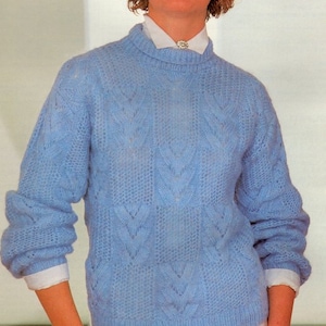 Può includere: Un maglione di lana blu chiaro con un motivo a treccia. Il maglione ha un collo rotondo e maniche lunghe.