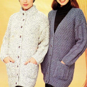 May include: Two women modelling knitted cardigans. One is a speckled white and grey with a high collar and button fastening. The other is a solid blue cardigan with a V-neck, button fastening, and pockets. Both cardigans are long-sleeved and have pockets.