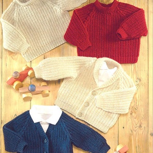 May include: Five knitted baby sweaters in different colours and styles. The sweaters are laid out on a wooden surface.