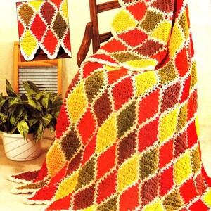 May include: A crocheted blanket with a diamond pattern in shades of red, yellow, green, and brown. The blanket is folded and draped over a wooden chair.