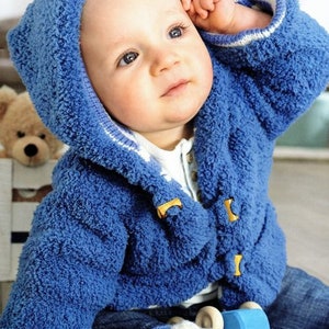 May include: A baby wearing a blue hooded jacket with yellow toggles and white trim. The jacket is made of a soft, textured material. The baby is also wearing blue jeans and has a toy nearby.