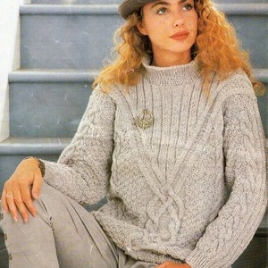 May include: A gray cable knit sweater with a V-neck and a decorative pin. The sweater is worn by a person wearing a brown fedora and gray pants.  ARAN 81-107cm 32-42inch